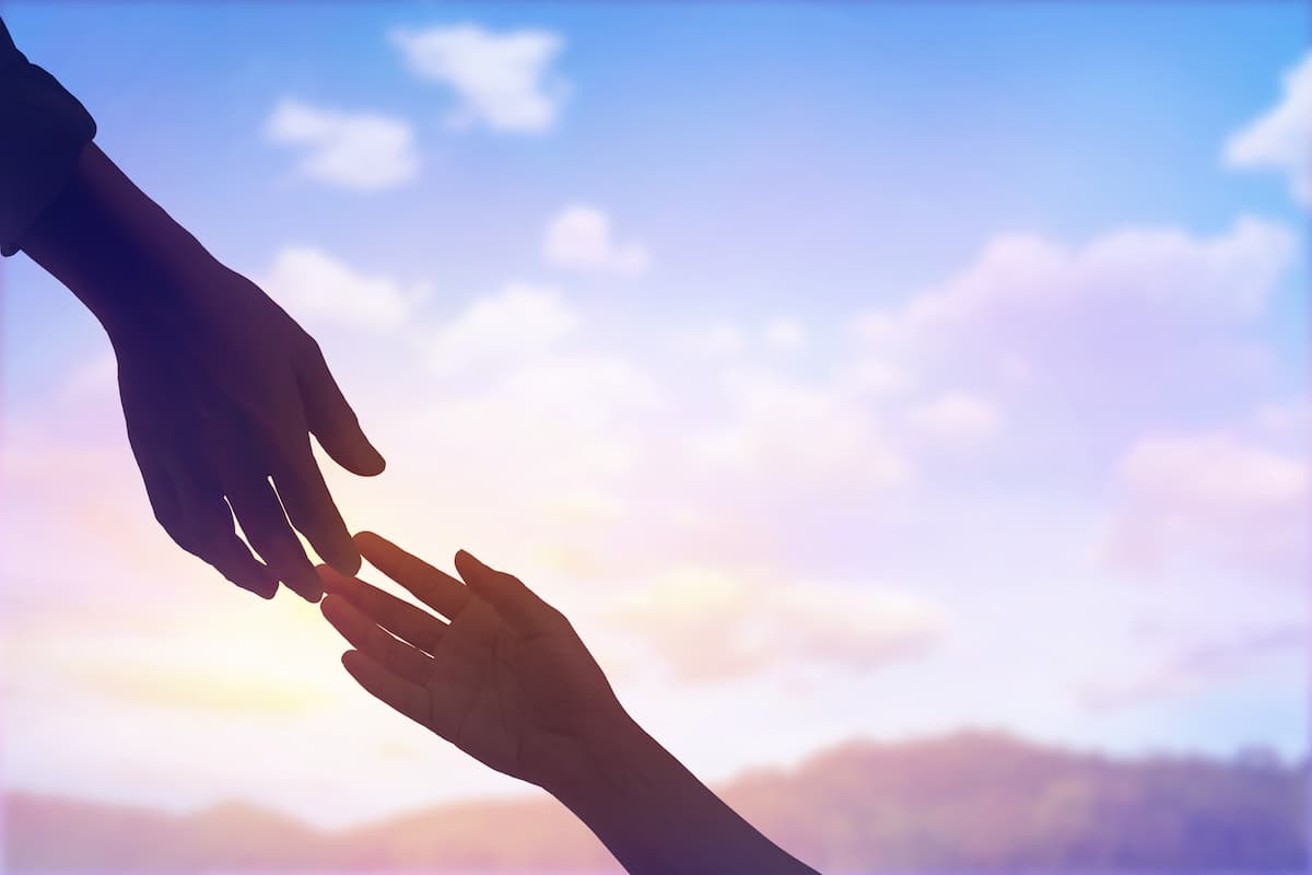 two hands touching against the sunset sky