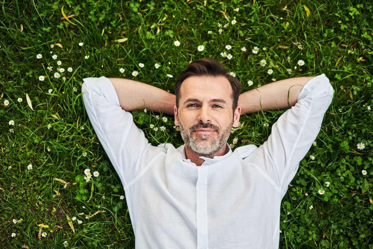 middle aged man in white dress shirt lying on the grass with daisies