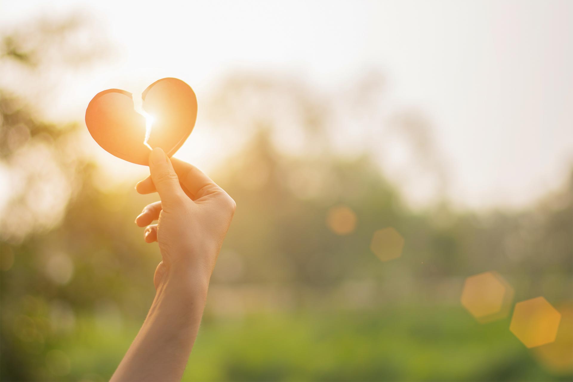 image of a broken red heart held by a hand with light shining through