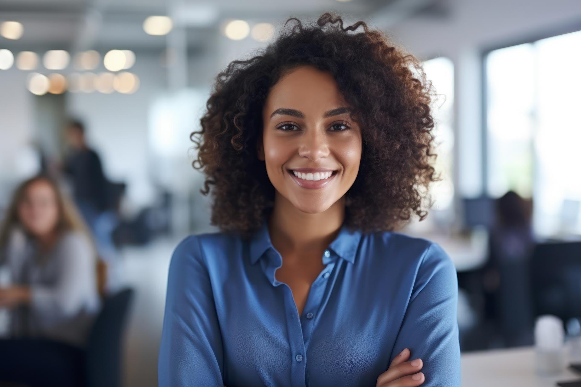 a smiling young woman with curly hair wearing blue top standing in the office environment